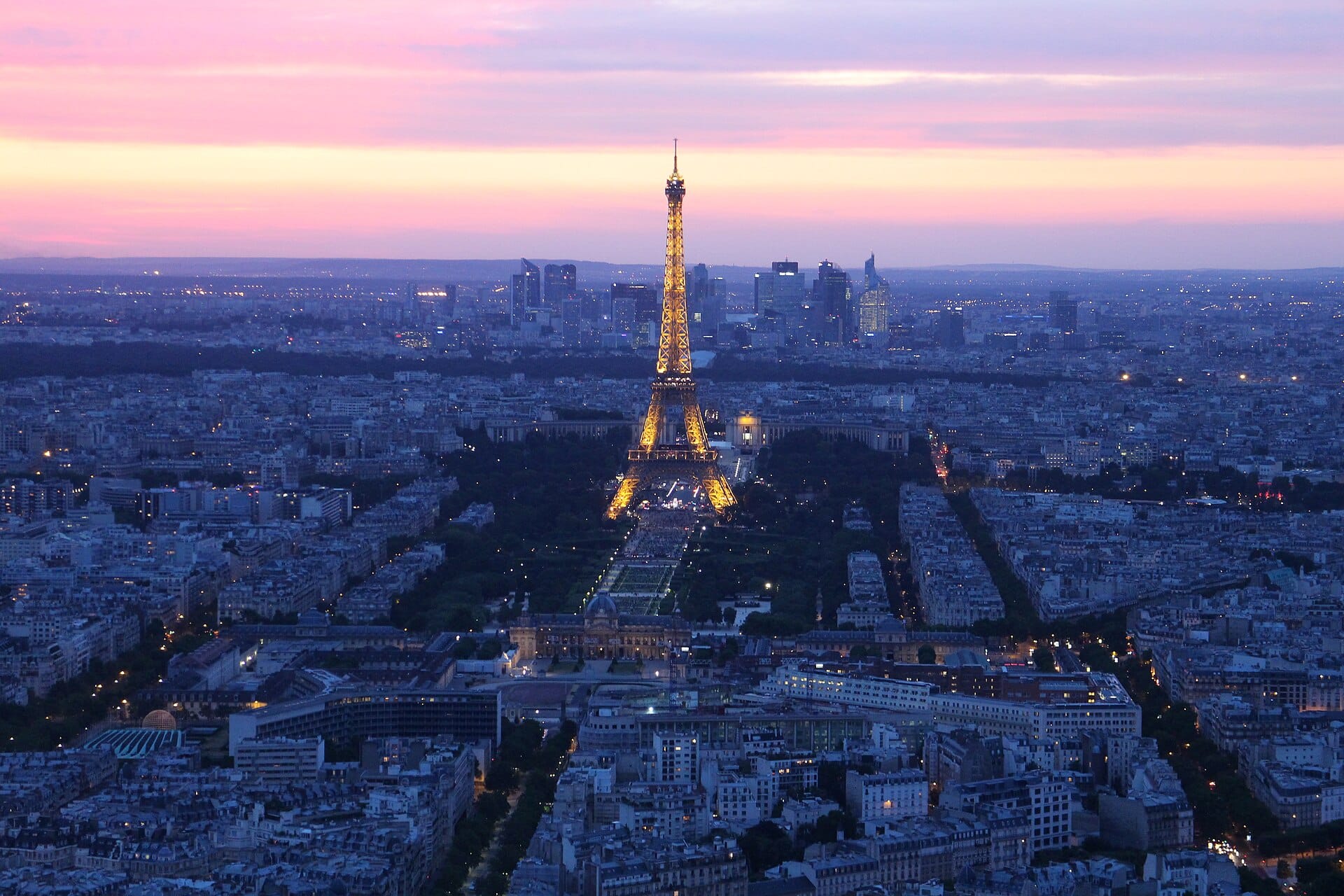 The Eiffel Tower lit at dusk above the rooftops of Paris